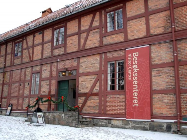 Besøkssenteret på Akershusfestning i en historisk bygning med rød murstein og bindingsverk, dekorert med julekranser, sett på en snødekt dag.
