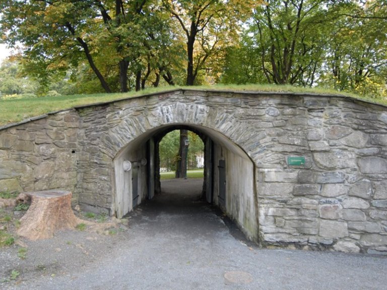 Steinbuegang med gresskledd topp i et parkområde med trær og grøntområder.