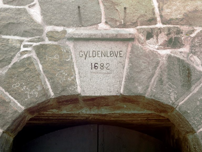 Steinbue med inskripsjonen 'GYLDENLØVE 1682' gravert på en rektangulær steinblokk over buen.