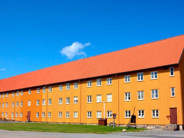 Lang, gul bygning med rødt tak og flere vinduer under en klar blå himmel.