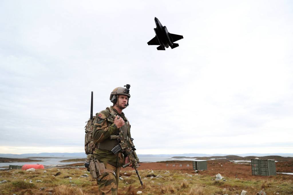 Bildet viser en soldat på et øvningsfelt for Forsvaret, i bakgrunnen flyr et F-35 kampfly. 